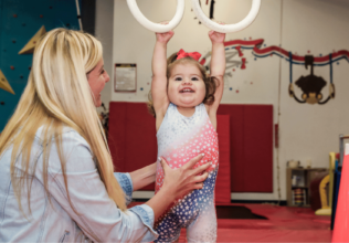 Smiling toddler with her mommy playing on the gymnastics hanging rings.