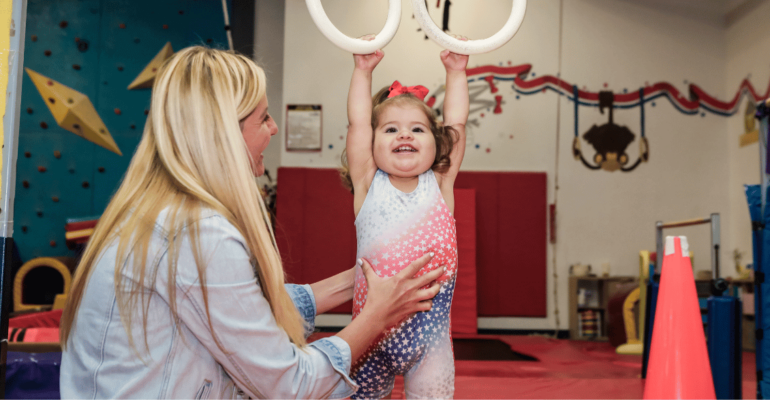 Smiling toddler with her mommy playing on the gymnastics hanging rings.